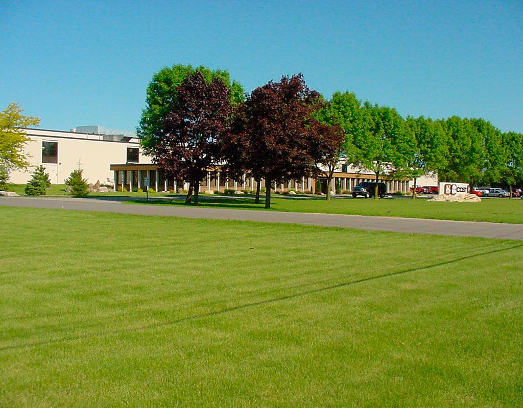 One of COST of Wisconsin's fabrication facilities - a large building with a lush green lawn and trees.