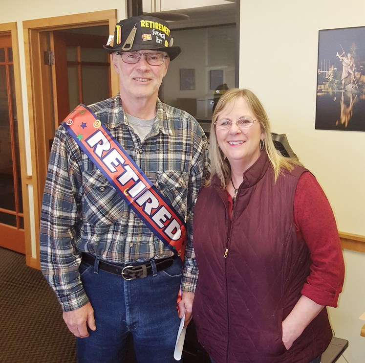 Jerry Elhke stands with his wife on his retirement day. He wears a party hat and a sash that says "retired" across his chest.