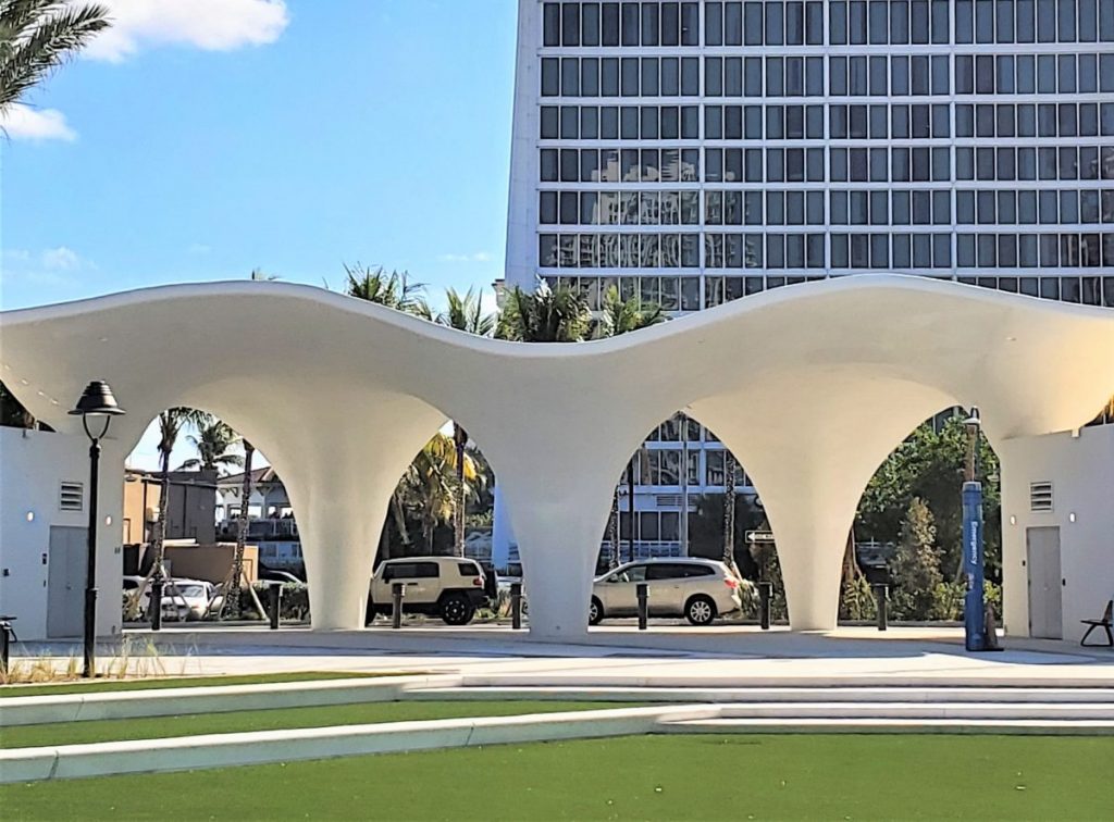 An architectural shotcrete Porte Cochere in Ft. Lauderdale is a large structure with pillars and a contemporary curving design that stands in a sunny community park.