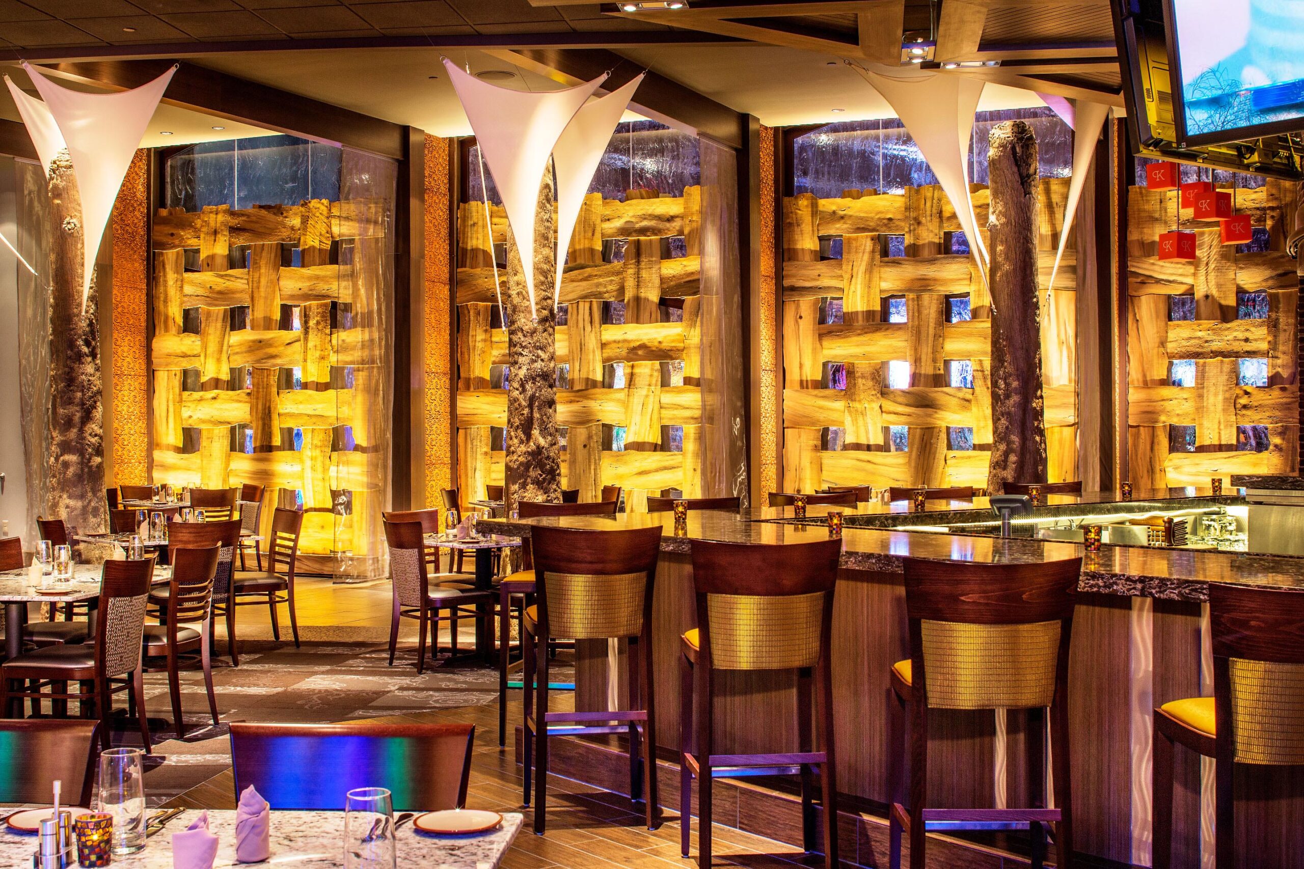 Ioc woven walls A casino bar and restaurant walls are adorned with intracate woven screens. The bar is lined with high-back bar chairs, and tables fill the dining room floor.