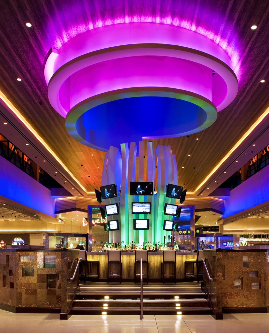 Cleo design Neon blue, purple and green lights spill from the ceiling onto the casino floor. A wall of televisions display Casino advertisements to the room.