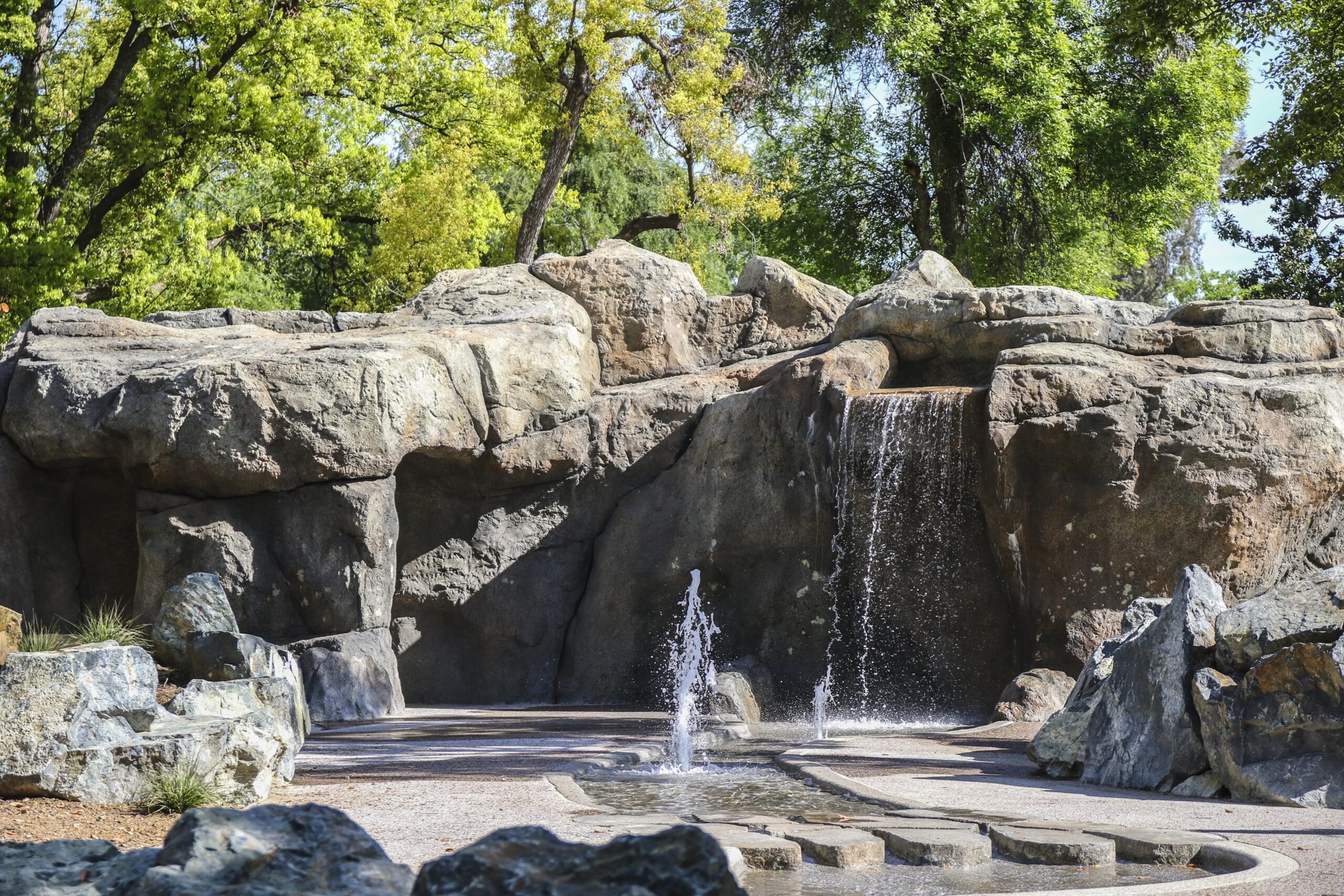 Wf 025 Large artificial rockwork cliffs with running waterfalls draining into shallow ponds in an outdoor park area.